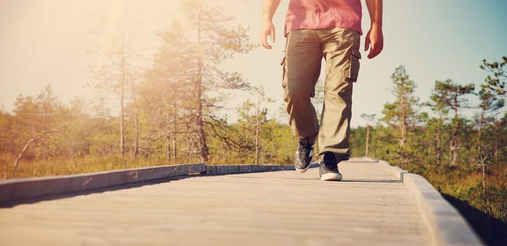 Man walking on wooden walkway in nature. Closeup of human feet in shoes