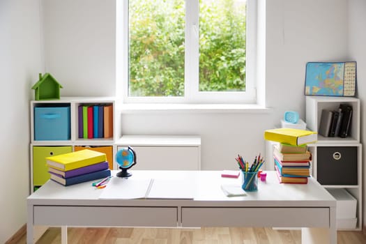 Colourful children rooom with white walls and furniture. Desk at home interior with a window