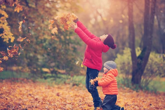 children throwing leaves in beautiful autumnal day. Boys playing outdoors in the park