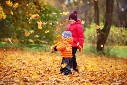 children throwing leaves in beautiful autumnal day. Boys playing outdoors in the park