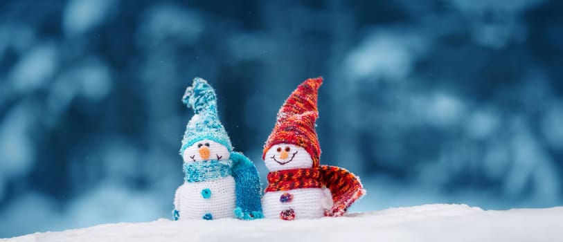 little knitted snowmans on soft snow on blue background