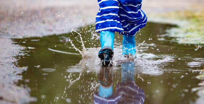Child walking in wellies in puddle on rainy weather. Boy under rain in summer