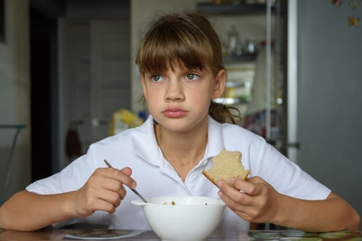 Girl thoughtfully eats soup at the table in the kitchen