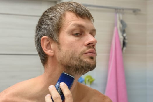 A man smooths his beard on his face with a hair clipper