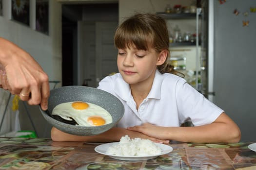 Mom cooked scrambled eggs for lunch and puts them from the pan on the daughter's plate