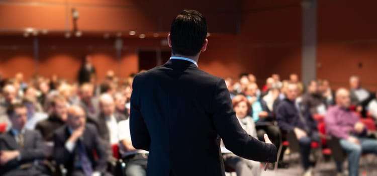Speaker giving a talk on corporate business conference. Unrecognizable people in audience at conference hall. Business and Entrepreneurship event.