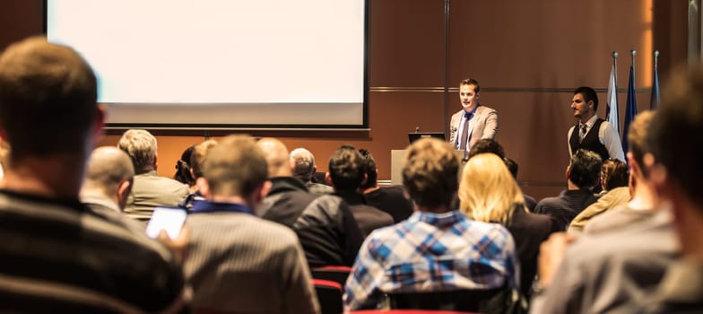 Speaker giving a talk in conference hall at business meeting event. Rear view of unrecognizable people in audience at the conference hall. Business and entrepreneurship concept.
