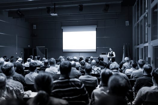 Speaker Giving a Talk at Business Meeting. Audience in the conference hall. Business and Entrepreneurship concept. Black and white blue toned image.