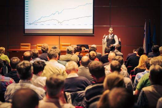 Speaker giving a talk in conference hall at business meeting event. Rear view of unrecognizable people in audience at the conference hall. Business and entrepreneurship concept.