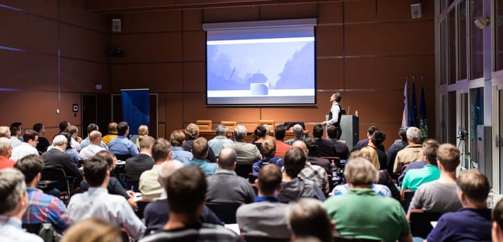 Speaker giving a talk in conference hall at business meeting event. Rear view of unrecognizable people in audience at the conference hall. Business and entrepreneurship concept.