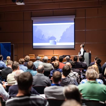 Speaker giving a talk in conference hall at business meeting event. Rear view of unrecognizable people in audience at the conference hall. Business and entrepreneurship concept.