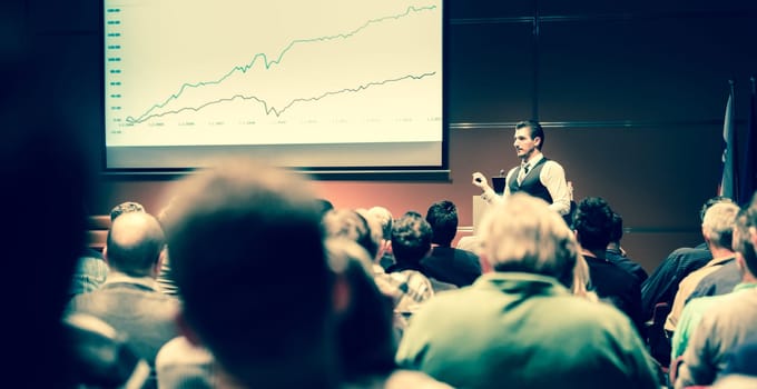 Speaker giving a talk in conference hall at business meeting event. Rear view of unrecognizable people in audience at the conference hall. Business and entrepreneurship concept.