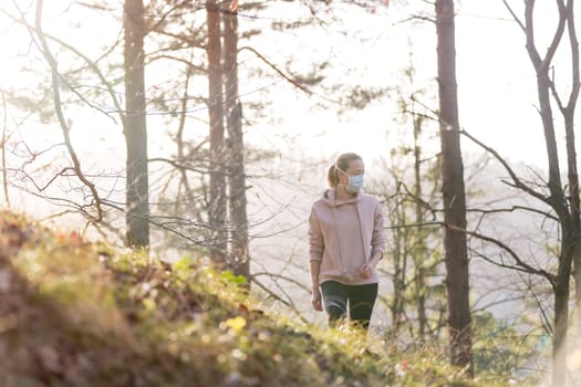 Portrait of caucasian sporty woman wearing a medical protection face mask while walking in the forest. Corona virus, or Covid-19, is spreading all over the world.