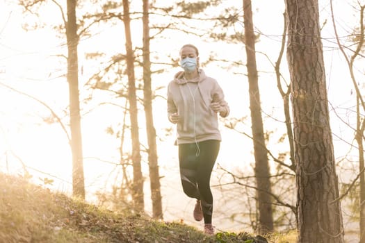 Portrait of caucasian sporty woman wearing a medical protection face mask while running in nature. Corona virus, or Covid-19, is spreading all over the world.