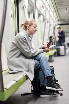 Portrait of lovely girl typing message on mobile phone in almost empty public subway train. Staying at home and social distancing recomented due to corona virus pandemic outbreak.