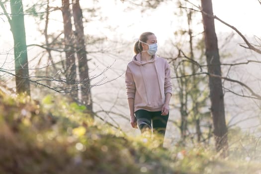 Portrait of caucasian sporty woman wearing a medical protection face mask while walking in the forest. Corona virus, or Covid-19, is spreading all over the world.