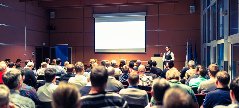 Speaker giving a talk in conference hall at business meeting event. Rear view of unrecognizable people in audience at the conference hall. Business and entrepreneurship concept.