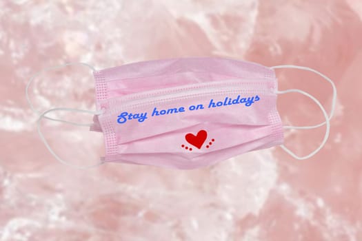 Closeup of two pink surgical masks for protection from covid-19 virus with the inscription stay home on holidays and a red heart on abstract bright background. Pandemic prevention.