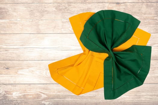 Top view of a folded yellow and green kitchen cloth, textile, tablecloth or napkin on blurred wooden background. Template for your food and product display montage.