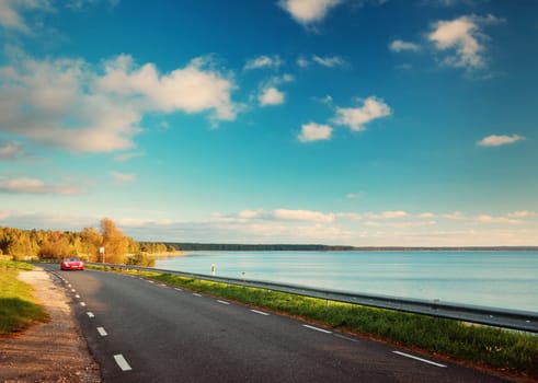 asphalt road with moving car at seaside at sunset