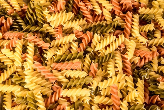 Background image of three different colours of fussili pasta.