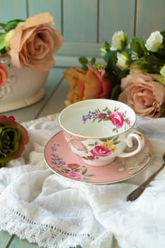 Porcelain vintage tea cup over wooden table with roses, vertical image