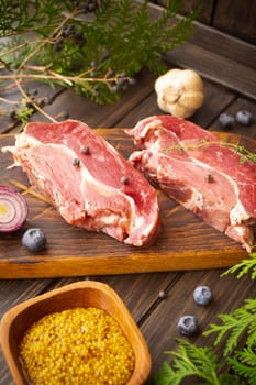 fresh meat of wild boar on the board for cutting with blueberries and a bulb of garlic, vertical image