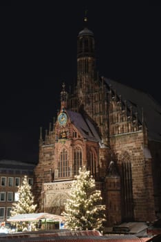 The Nuremberger Frauenkirche on the main market at night during Christmas tine and Christmas trees with snow.