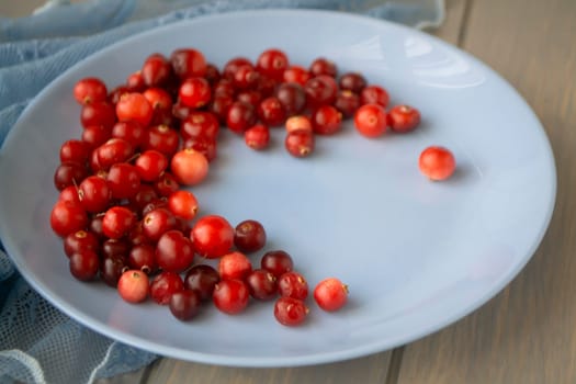 blue plate of cowberries on old wooden table, close up
