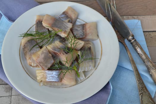 Pieces of herring with onions and dill on old plate in russian style close up