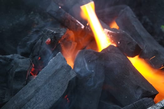 Fire on logs in fire pot with embers and burning coal. Bonfire with blazing red and orange fire flames. Fire background with woods and planks on fire at night view.
