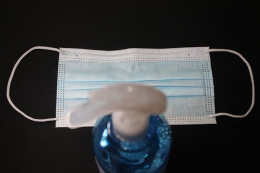 blue color cloth face mask with hand sanitizer bottle isolated on black background