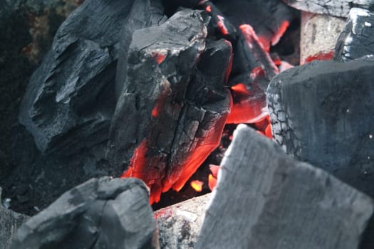 Fire on logs in fire pot with embers and burning coal. Bonfire with blazing red and orange fire flames. Fire background with woods and planks on fire at night view.