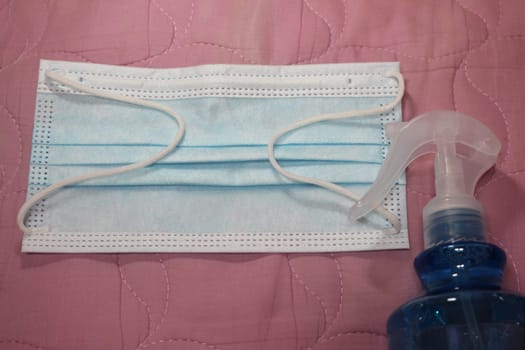 blue color cloth face mask with hand sanitizer bottle isolated on pink background