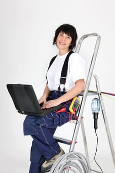 Female electrician sat on ladder with laptop