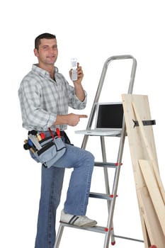 Carpenter standing by a ladder with  a mobile telephone