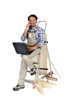 Carpenter perched on ladder whilst making a telephone call