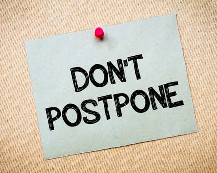 Recycled paper note pinned on cork board.Don' t Postpone Message. Motivational Concept Image