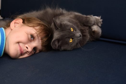 The girl pressed her head to the cat lying on the sofa