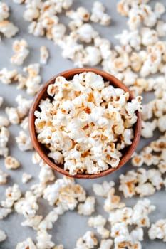 A wooden bowl of salted popcorn from above on grey table. Selective focus and copyspace for text. Concept of relax and time off. Vertical orientation.