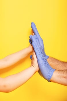 Hands gestures. the palms of the child and the father against each other as a sign of agreement, in latex glove over yellow background. Vertical orientation