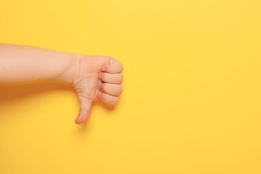 Hands gestures. Baby hand showing symbol of disagreement isolated on yellow background with copy space