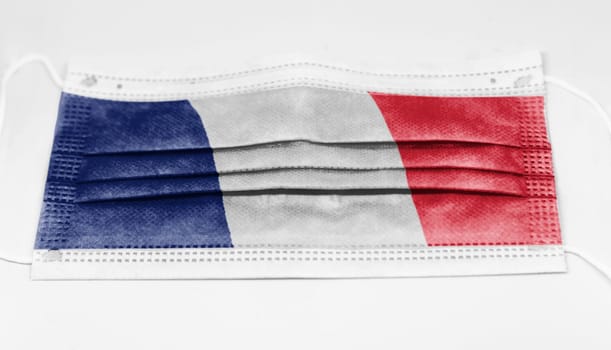 The national flag of France printed on a disposable surgical mask. Coronavirus covid-19 pandemic prevention and protection. Health and medicine