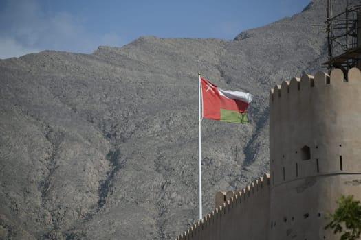 The Nakhal Nakhl Fort is a large fortress at the foot of the Hadshar Mountains in the Al Batinah region of Oman. An Omani flag flies in front of the fortifications.