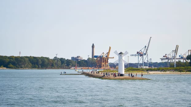 Tourists at the mill beacon, the landmark of the city of Swinoujscie, in the background the harbour