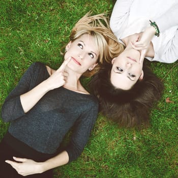 Two thoughtful girls lying in the grass have an smart idea.