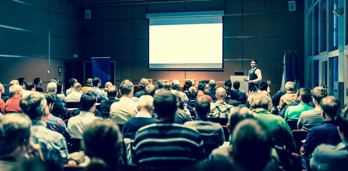 Speaker giving a talk in conference hall at business meeting event. Rear view of unrecognizable people in audience at the conference hall. Business and entrepreneurship concept.