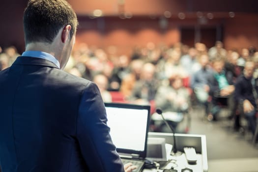 Speaker at Business Conference with Public Presentations. Audience at the conference hall. Entrepreneurship club. Rear view. Panoramic composition. Background blur.