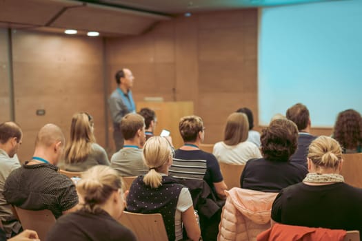 Speaker Giving a Talk at Business Meeting. Audience in the conference hall. Business and Entrepreneurship. Focus on unrecognizable people from rear.