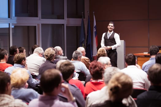 Speaker giving a talk in conference hall at business meeting event. Rear view of unrecognizable people in audience at the conference hall. Business and entrepreneurship concept.